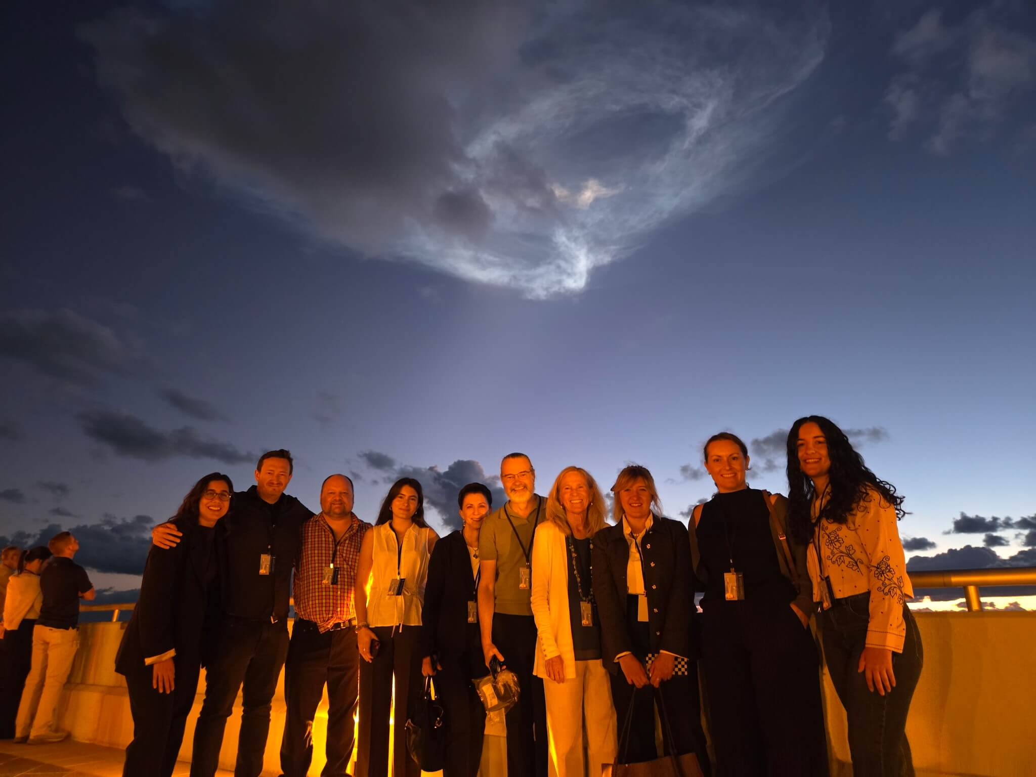 The extended NSCF team, including advisors and partners, Axiom Space, BioServe Space Technologies, Leo Biosciences, Confluent Horizons and Genomics Consult, taken on the balcony at Kennedy Space Center OSB II (Operations Support Building II) shortly after the launch of SpaceX CRS-35, with the plume still visible behind them. Photo Courtesy of NSCF.